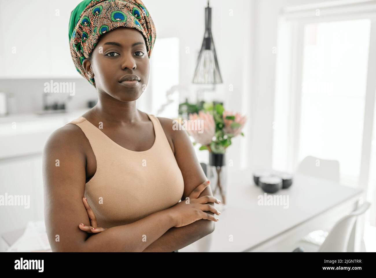 Portrait of a confident Black African woman with her arms crossed looking into the camera. Working from home and wearing a traditional headscarf Stock Photo