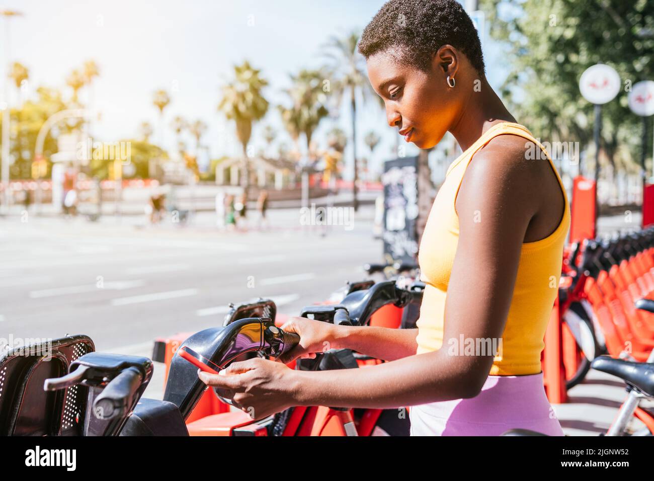 trendy african american woman using her phone to unblock bike from a bike rack Stock Photo