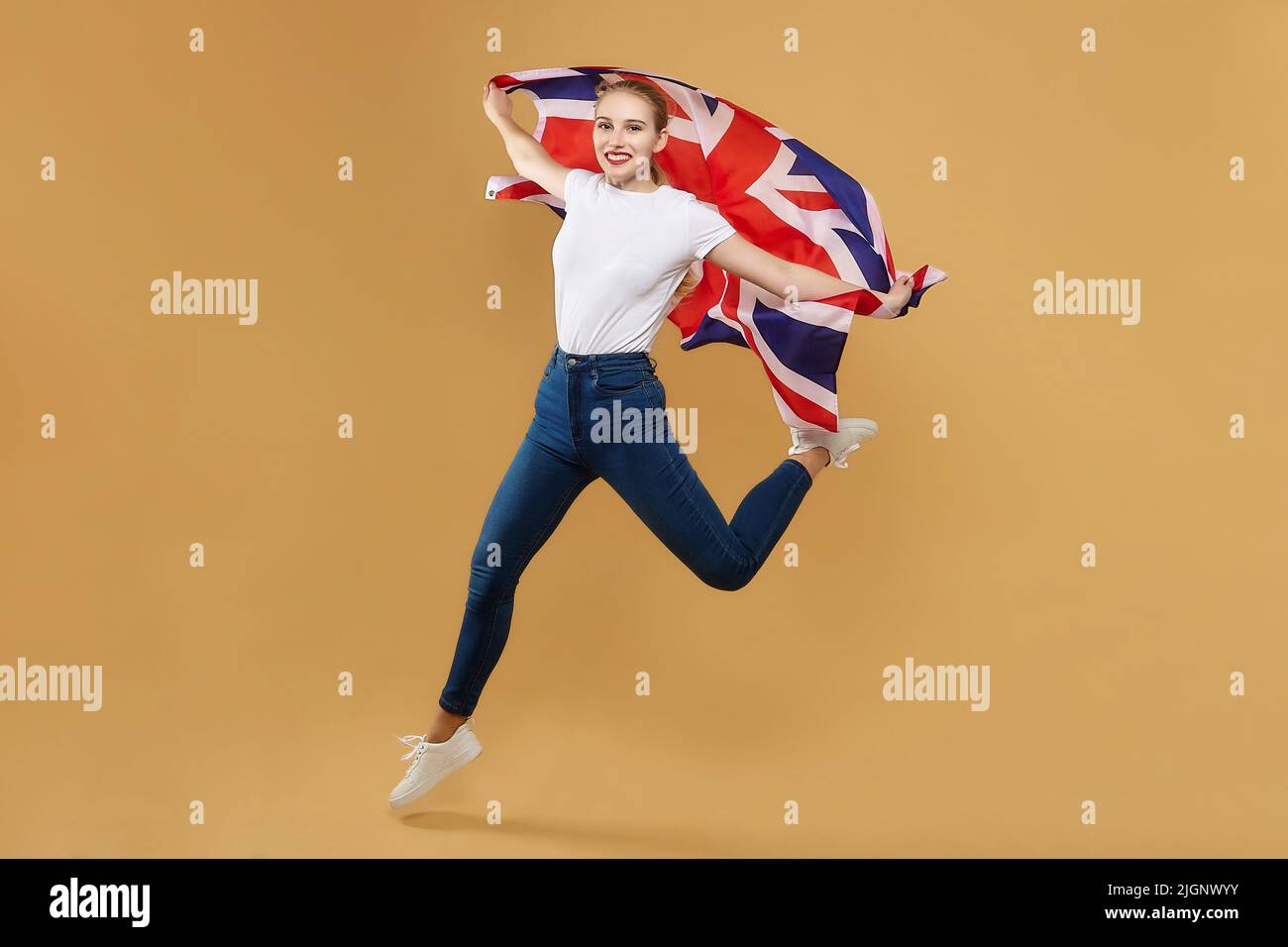 attractive blonde made a jump with a British flag. photo shoot in the studio with a yellow background. Stock Photo