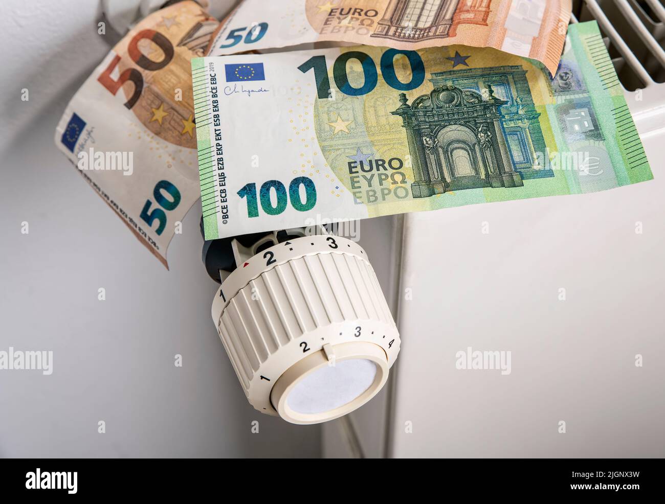 Radiator and thermostat with euro banknotes as a symbol for rising heating costs Stock Photo