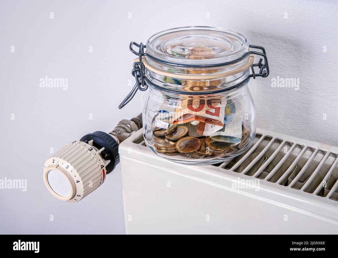 Saving for heating: radiator and thermostat with piggy bank and money Stock Photo