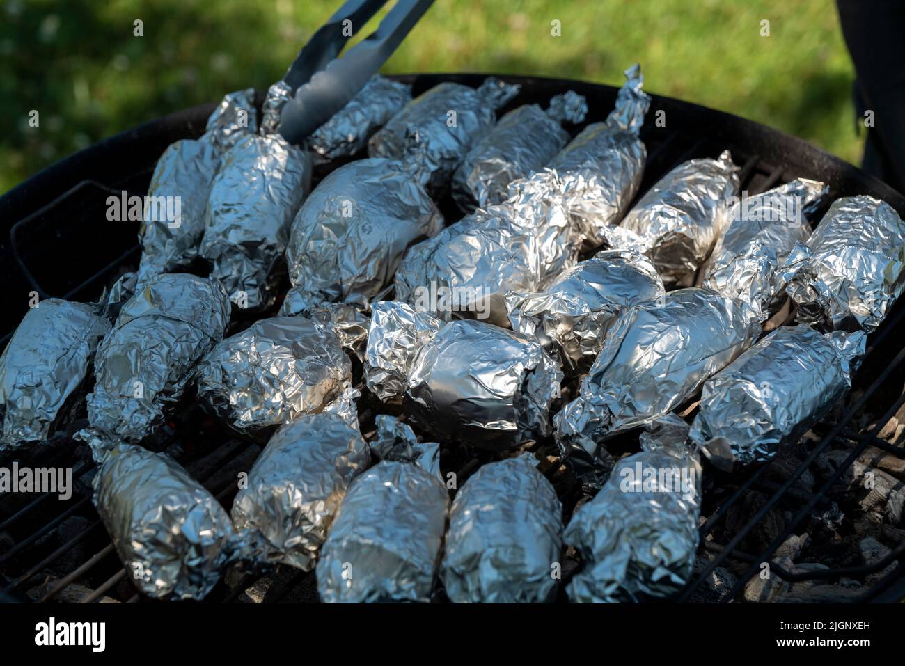 Home cooking Unwrapping corn being baked or cooked on firewood grill wrapped in aluminum foil