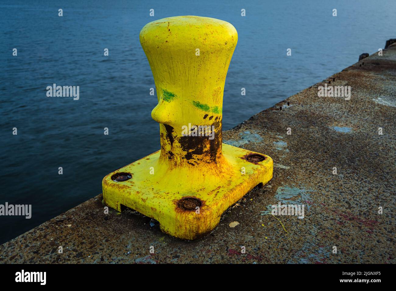 Yellow-colored mooring bollard is located on the edge of the quay and is visible against the water. There is no rope on this bollard Stock Photo
