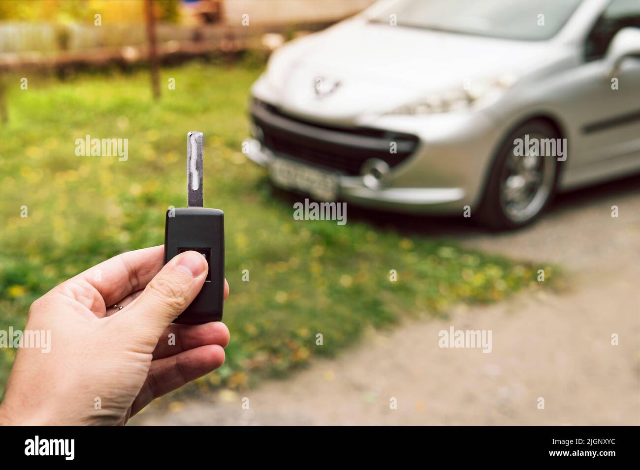 Man's hand pushes a button on the car remote control against parked blurred car. Vehicle key in male hand outsides. Unlocking vehicle by remote key si Stock Photo