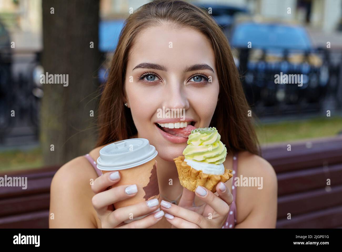 attractive girl with long hair holds a cake and a paper cup of coffee ...