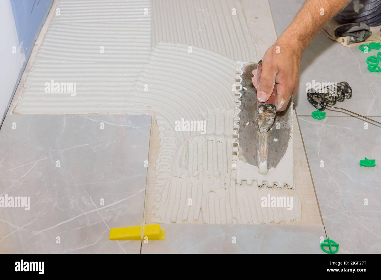 In preparation for laying tiles, mortar is troweled on a concrete floor