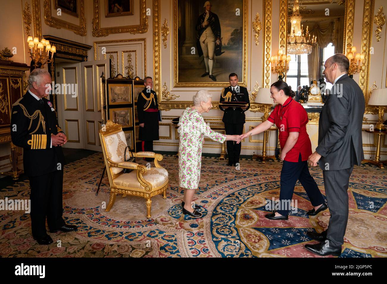 Queen Elizabeth II accompanied by the Prince of Wales, presenting the George Cross to representatives of the National Health Service Mr Peter May, Permanent Secretary at the Department of Health and Chief Executive of Health and Social care, and Sister Joanna Hogg, Royal Victoria Hospital Emergency Department, during an Audience at Windsor Castle, Berkshire. Picture date: Tuesday July 12, 2022. Stock Photo