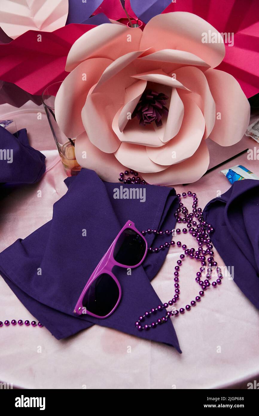 Party favors on table at wedding with large paper flower, purple sunglasses and purple napkins. Stock Photo