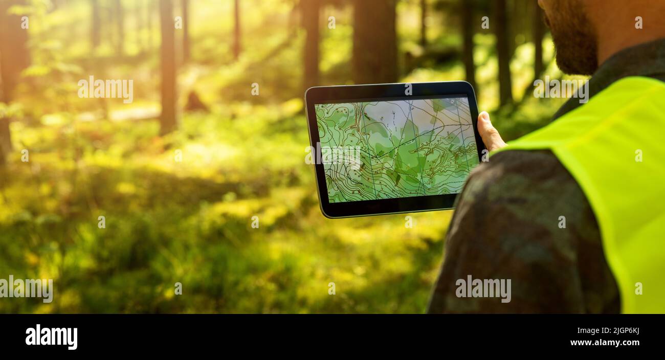 man working with topographic map data on digital tablet in forest. banner with copy space Stock Photo