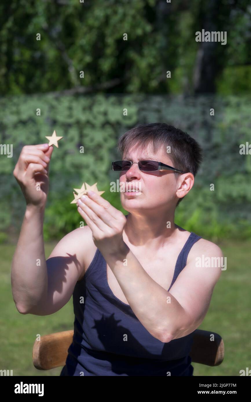 Woman sitting outdoor at summer in the garden and holding small wooden stars, survey concept. Stock Photo
