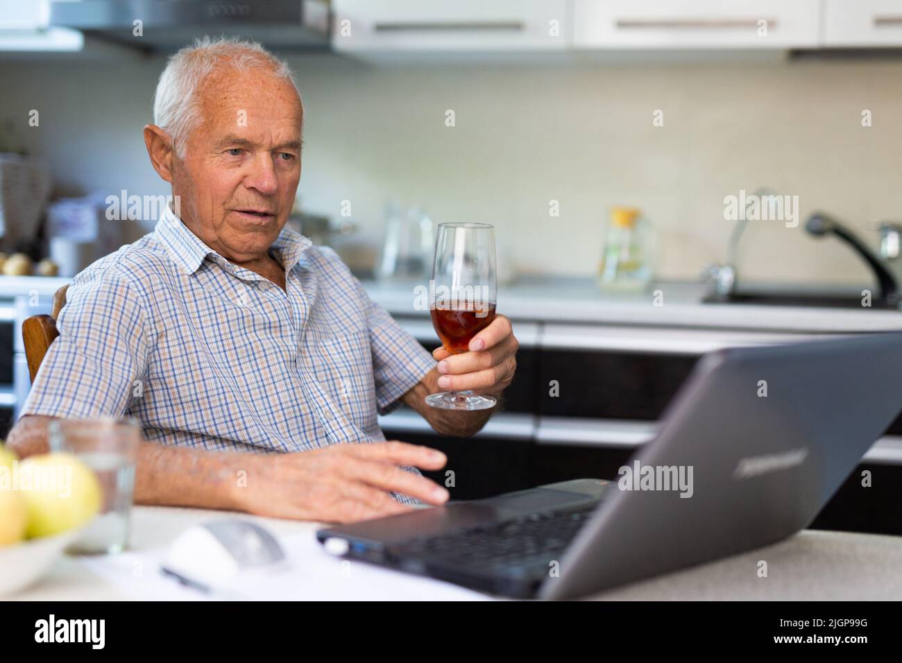 Senior man with glass of brandy and laptop Stock Photo