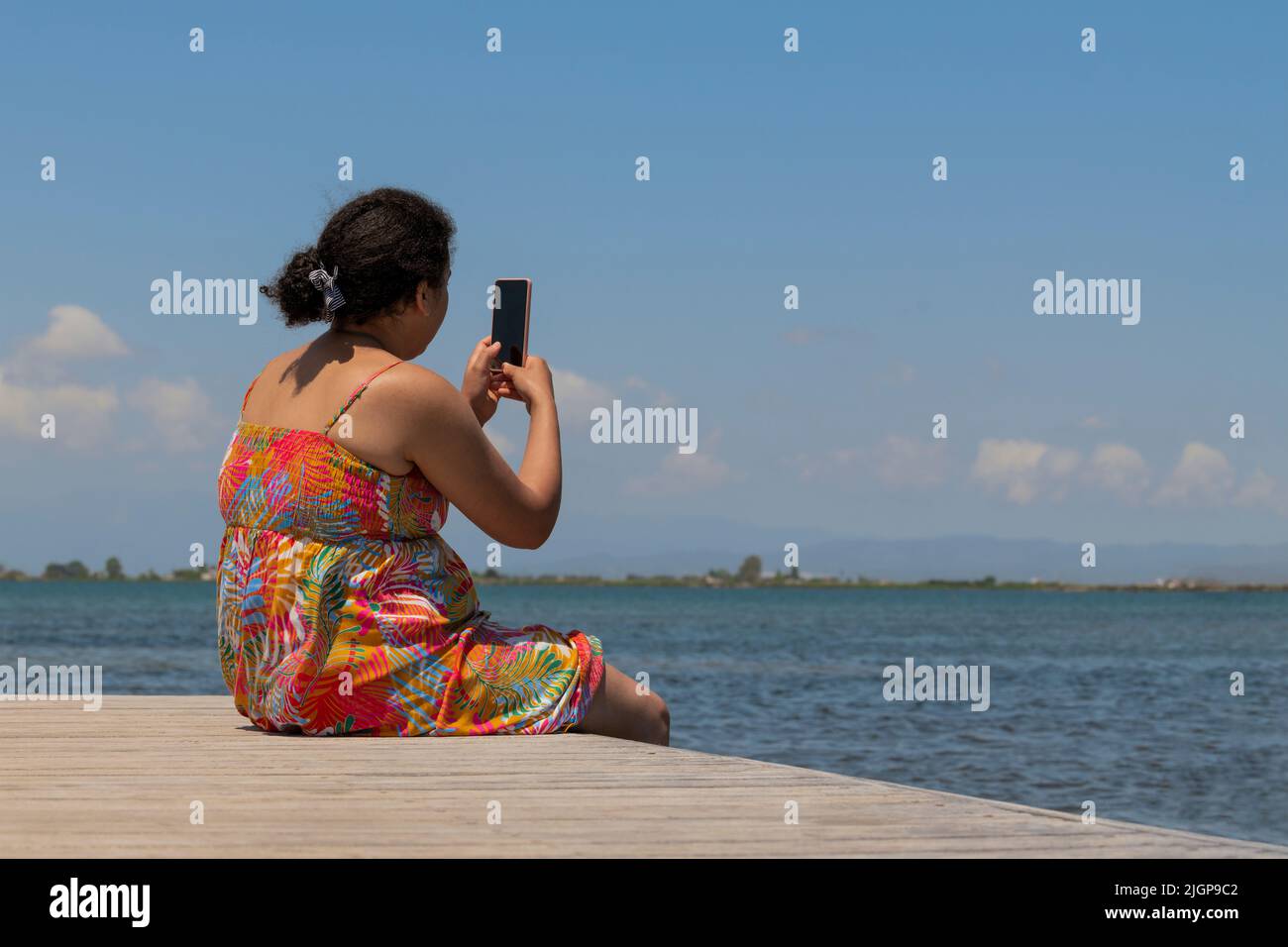 Woman sitting on a pontoon bridge using her phone Stock Photo