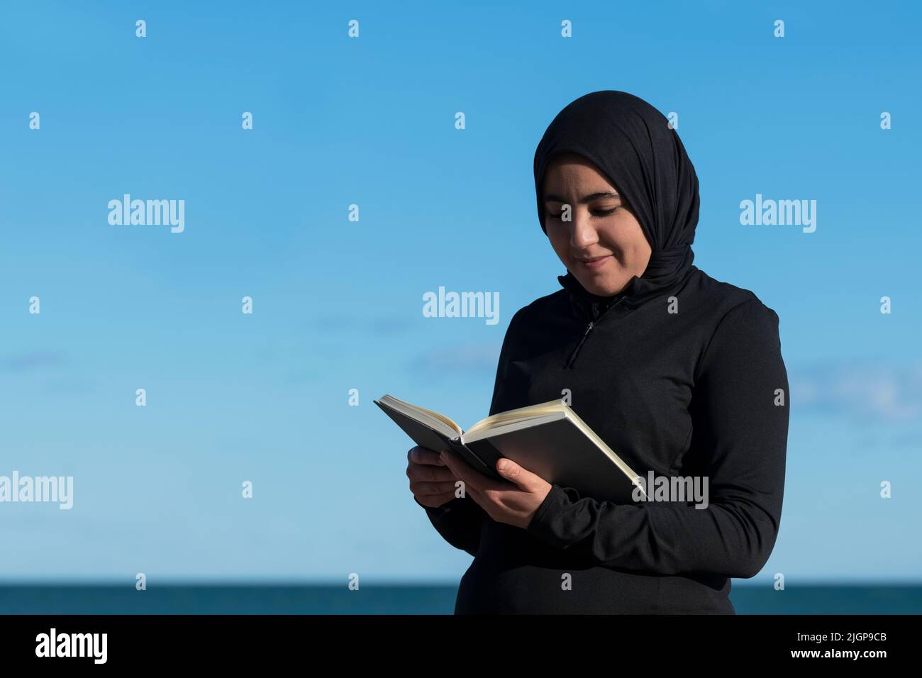 Muslim woman with a hijab reading a book outdoors. Stock Photo