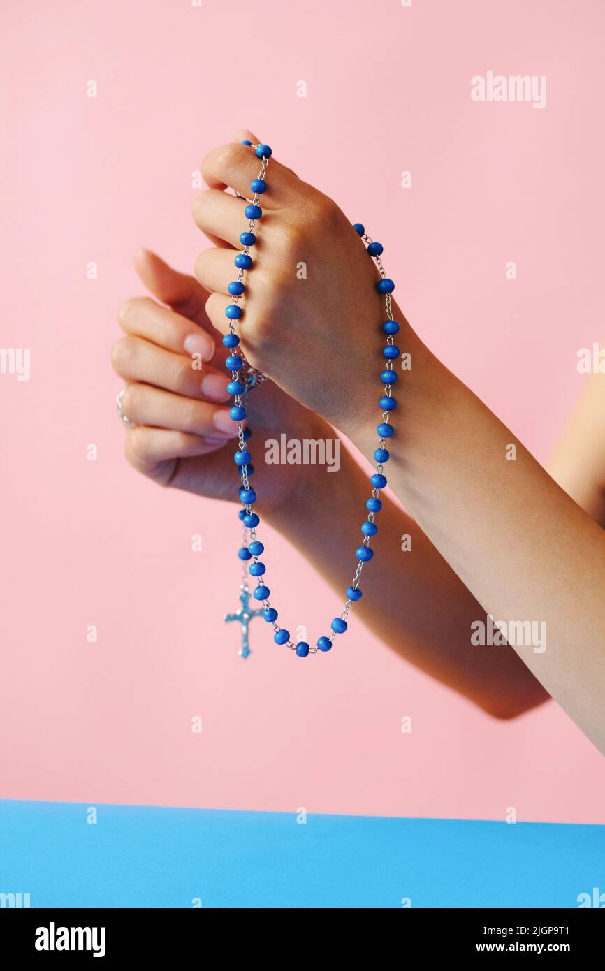 closeup hands with rosary praying in front of pink background Stock Photo