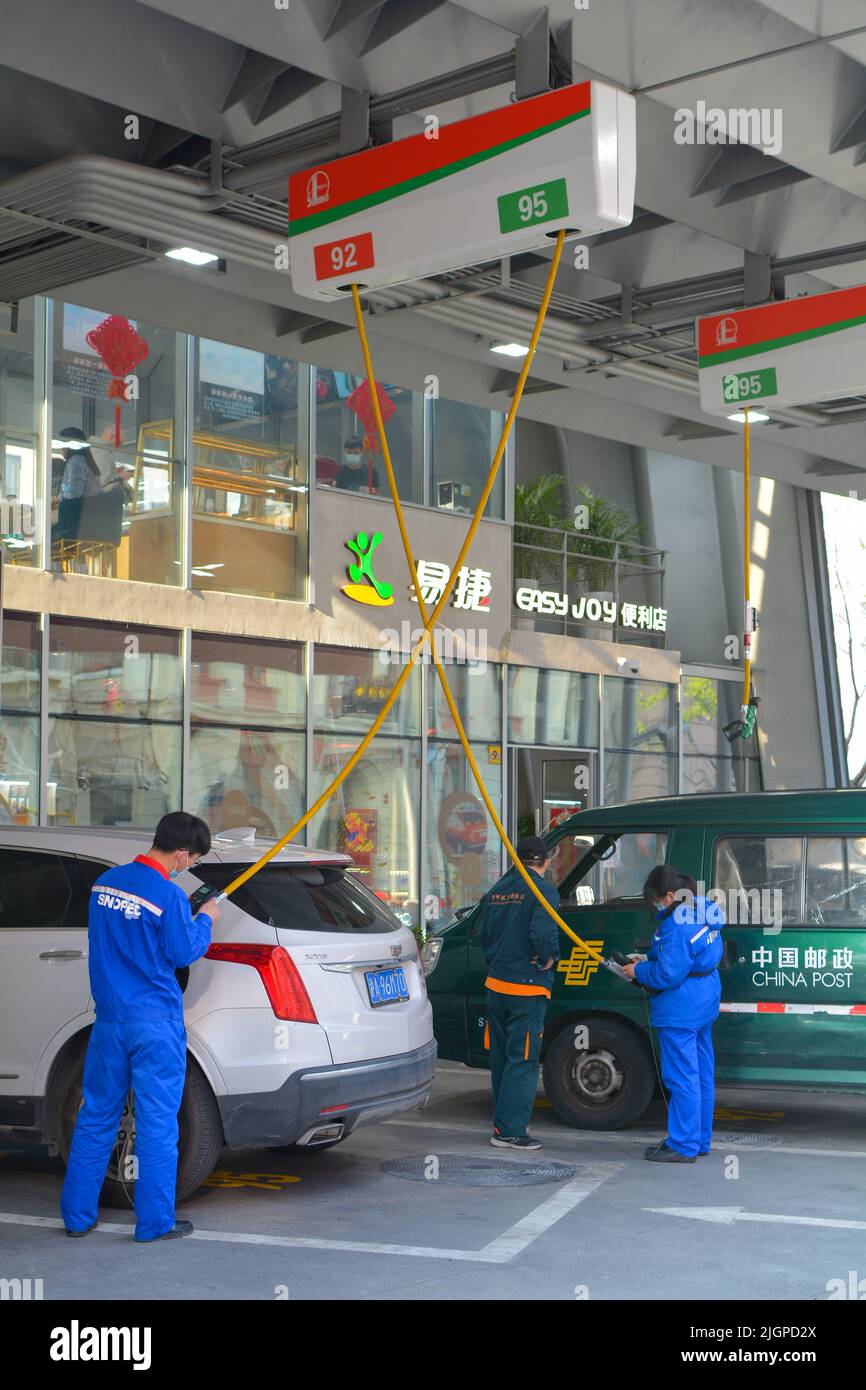 Sinopec petrol station in Shanghai, car and a van refuelling with attendants using overhead hoses. Stock Photo