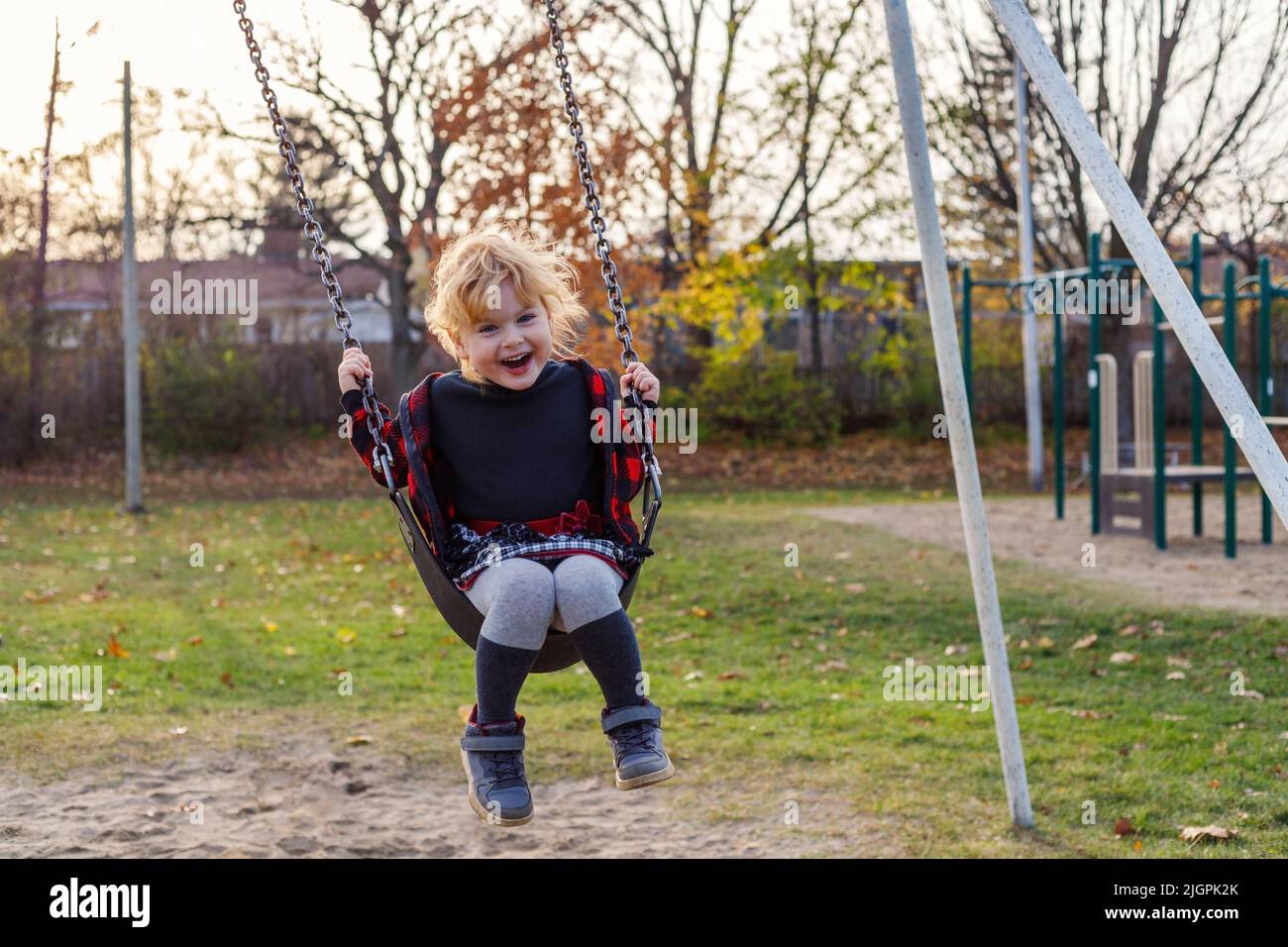 Smiling happy girl on swing in park in autumn. Girl at playground in fall season. Stock Photo