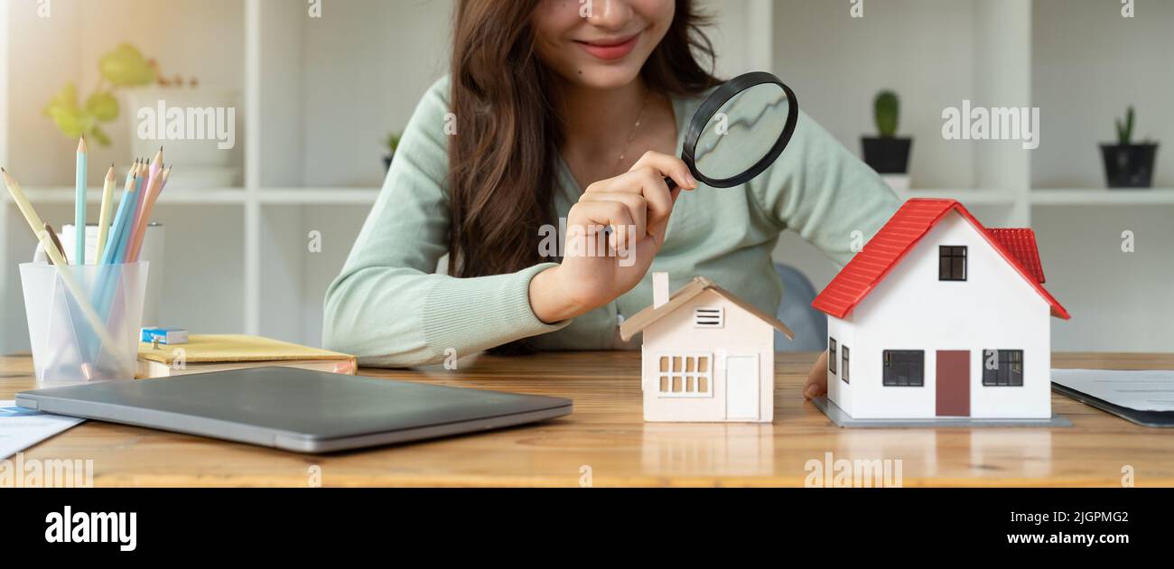 Looking for real estate agency, property insurance, mortgage loan or new house. Woman with magnifying glass over a wooden house at her office Stock Photo