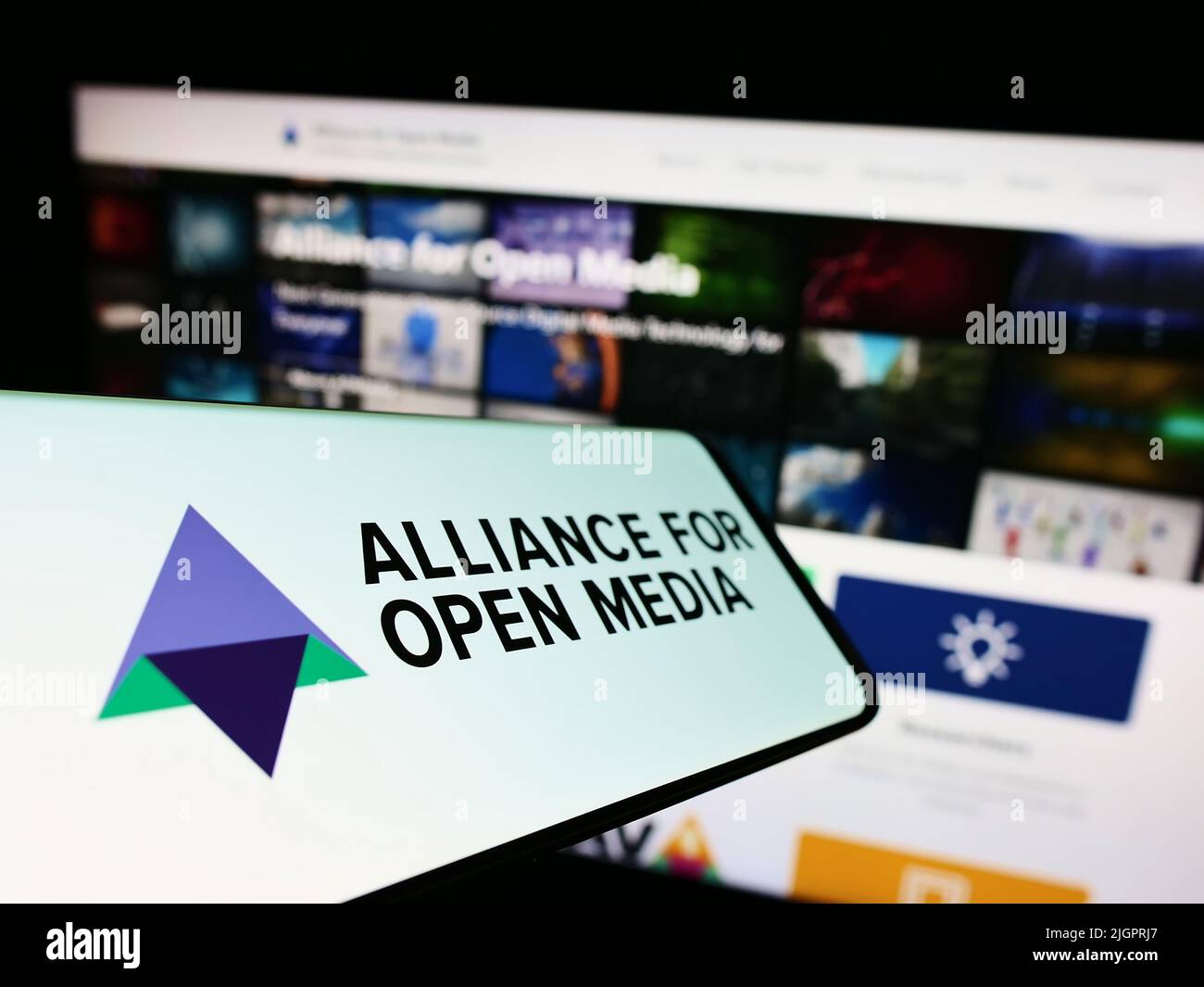 Mobile phone with logo of consortium Alliance for Open Media (AOMedia) on screen in front of website. Focus on center-left of phone display. Stock Photo