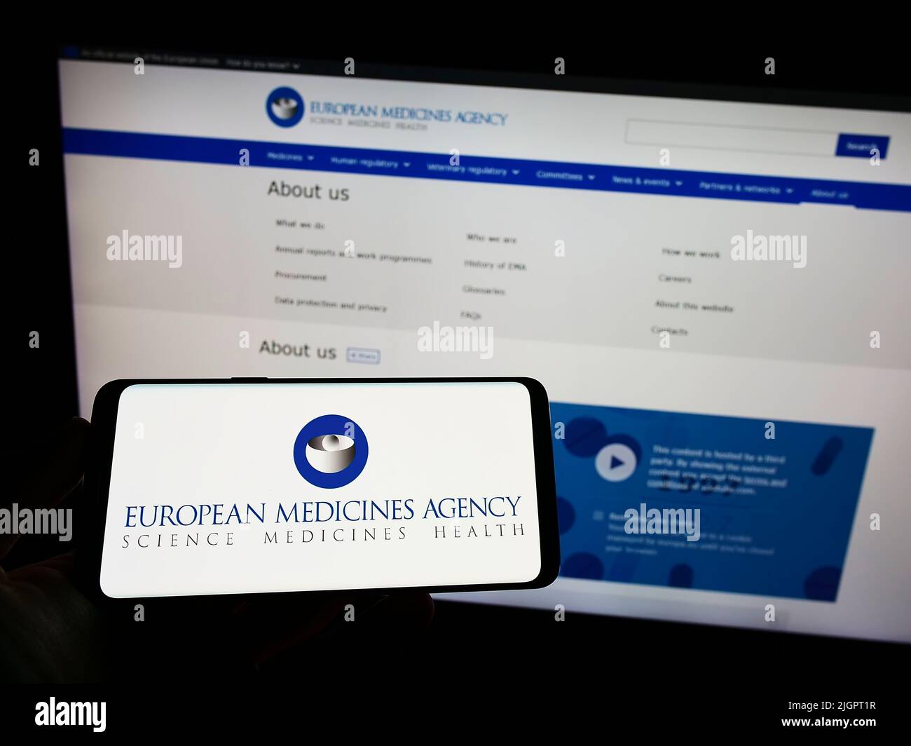 Person holding smartphone with logo of EU agency European Medicines Agency (EMA) on screen in front of website. Focus on phone display. Stock Photo