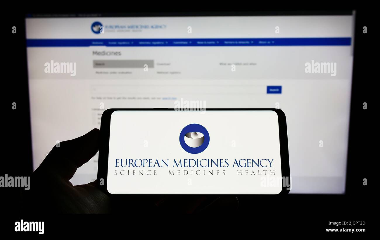 Person holding cellphone with logo of EU agency European Medicines Agency (EMA) on screen in front of webpage. Focus on phone display. Stock Photo