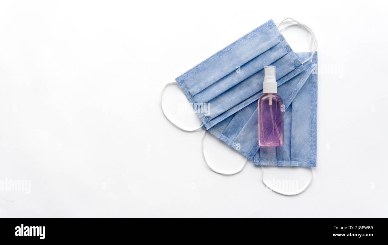 Close-up of COVID-19 and viruses protective tools. Three blue medical masks and purple sanitizer gel. Isolated on a white background. Coronavirus theme.  Stock Photo