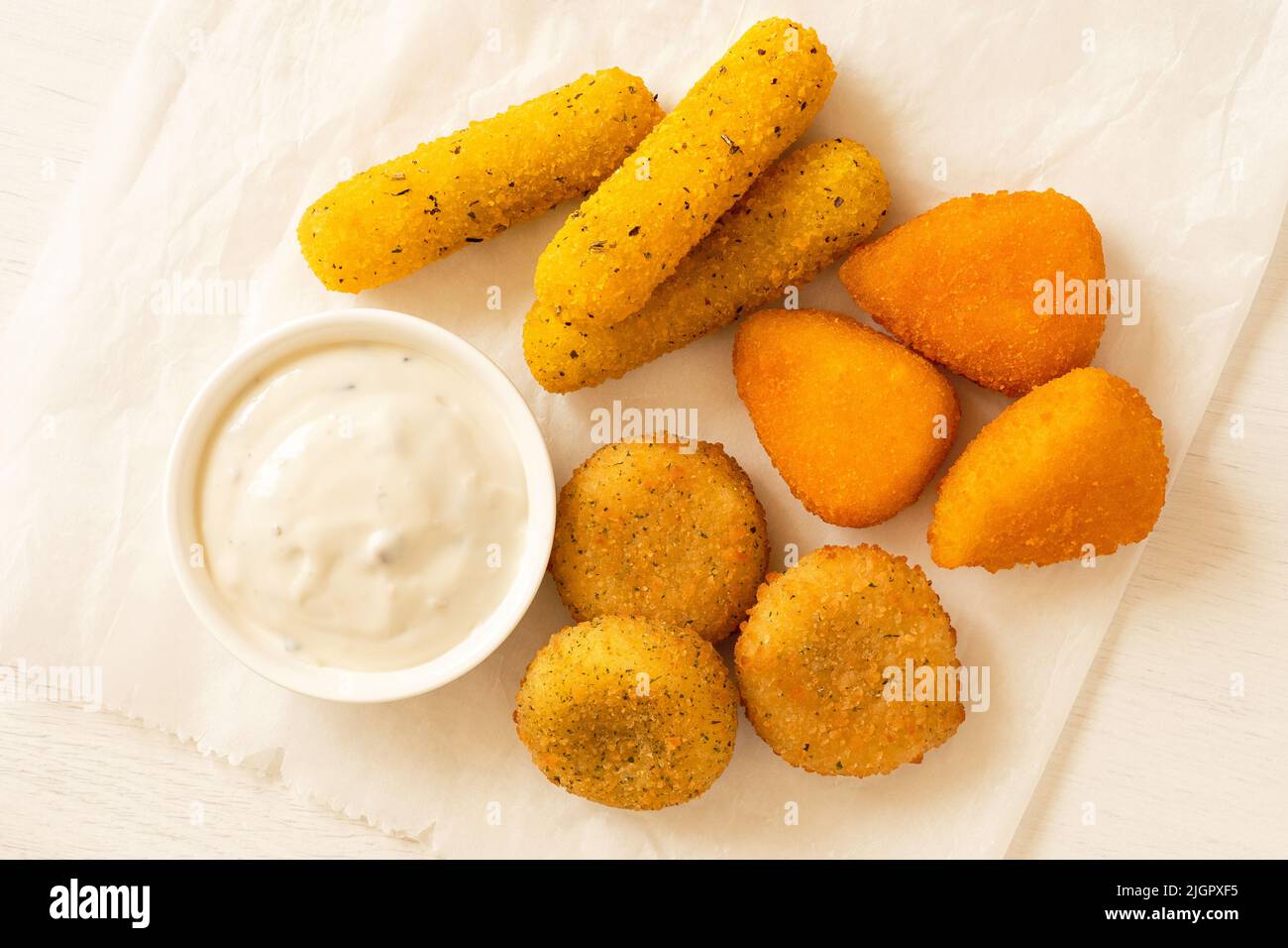 Selection of breaded fried cheese on a white baking paper with white dip isolated on white. Top view. Stock Photo