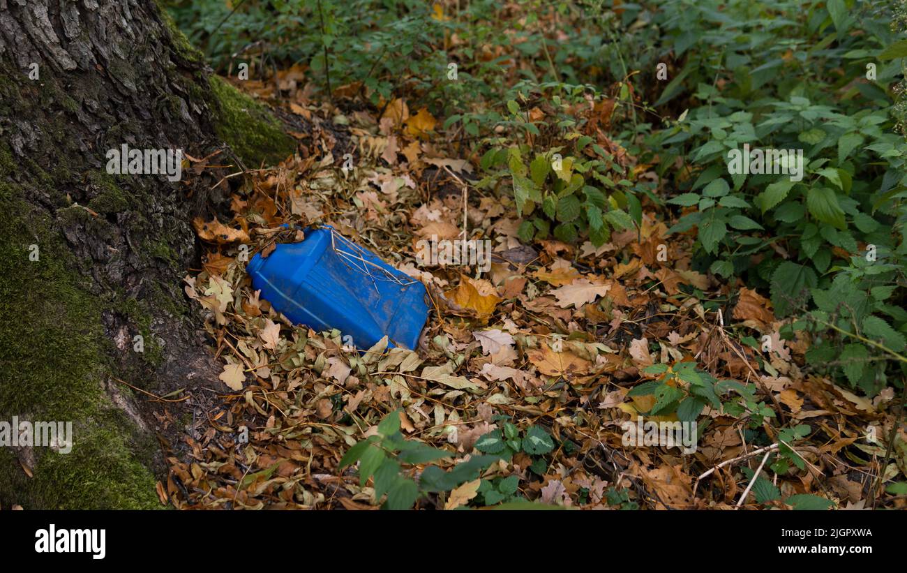 Environmental pollution. An old blue plastic canister from gasoline lies in the forest by a tree among the leaves. Toxicity. Soil contamination with hydrocarbons. Ecology. Stock Photo