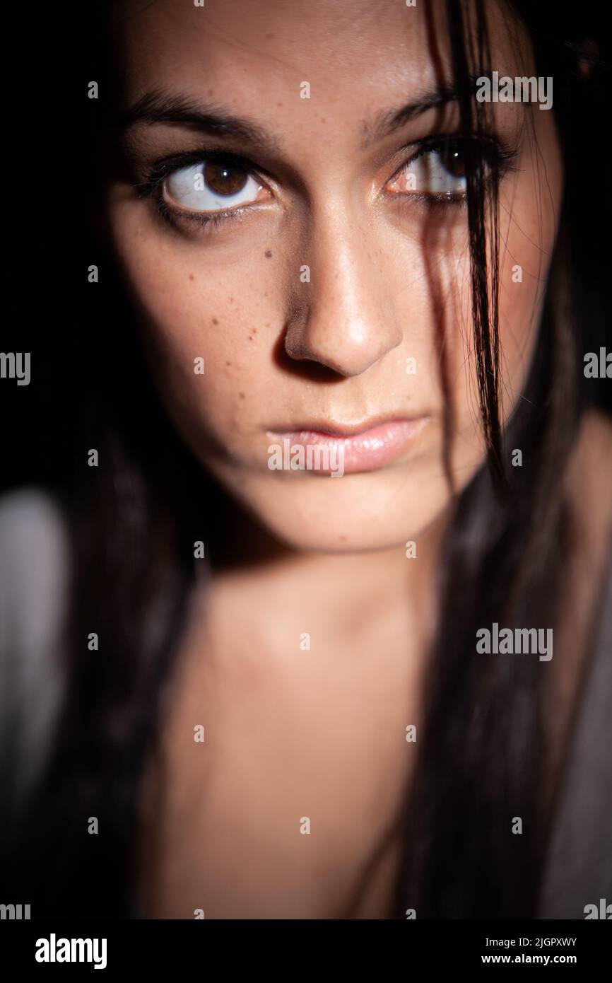 Dark Anxiety. A worried look on the face of a beautiful young mixed-race Anglo-Indian female model in a dark place. From a series with the same model. Stock Photo