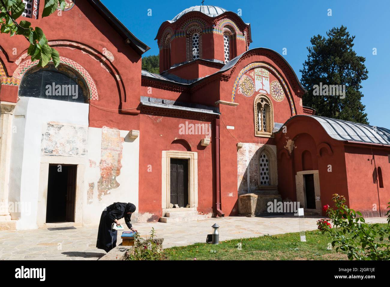 A female monk in black habit ironing some clothes outside the medieval Serbian Orthodox  'Patriarchate of Peć' Monastery in Kosovo. Stock Photo