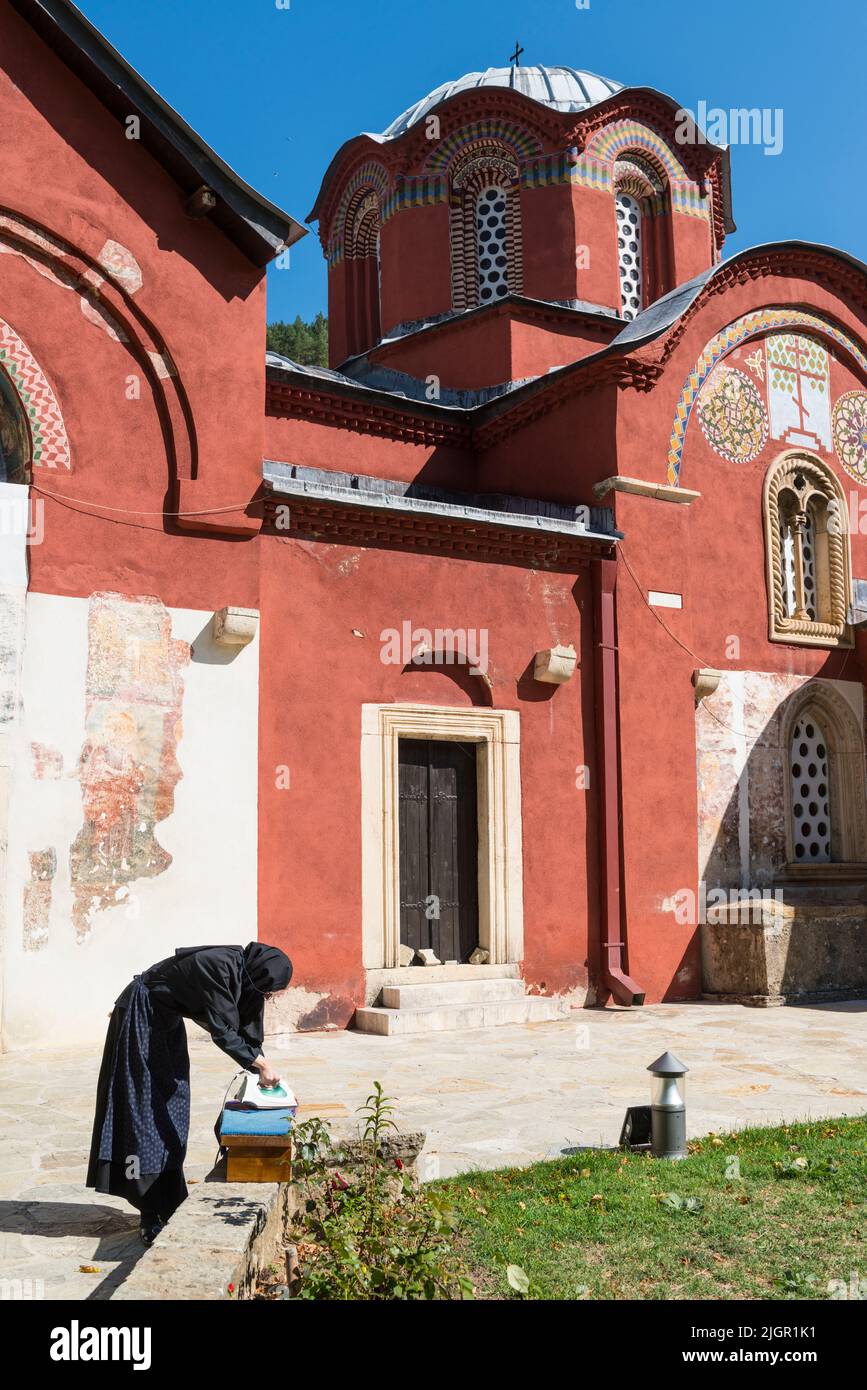 A female monk in black habit ironing some clothes outside the medieval Serbian Orthodox  'Patriarchate of Peć' Monastery in Kosovo. Stock Photo