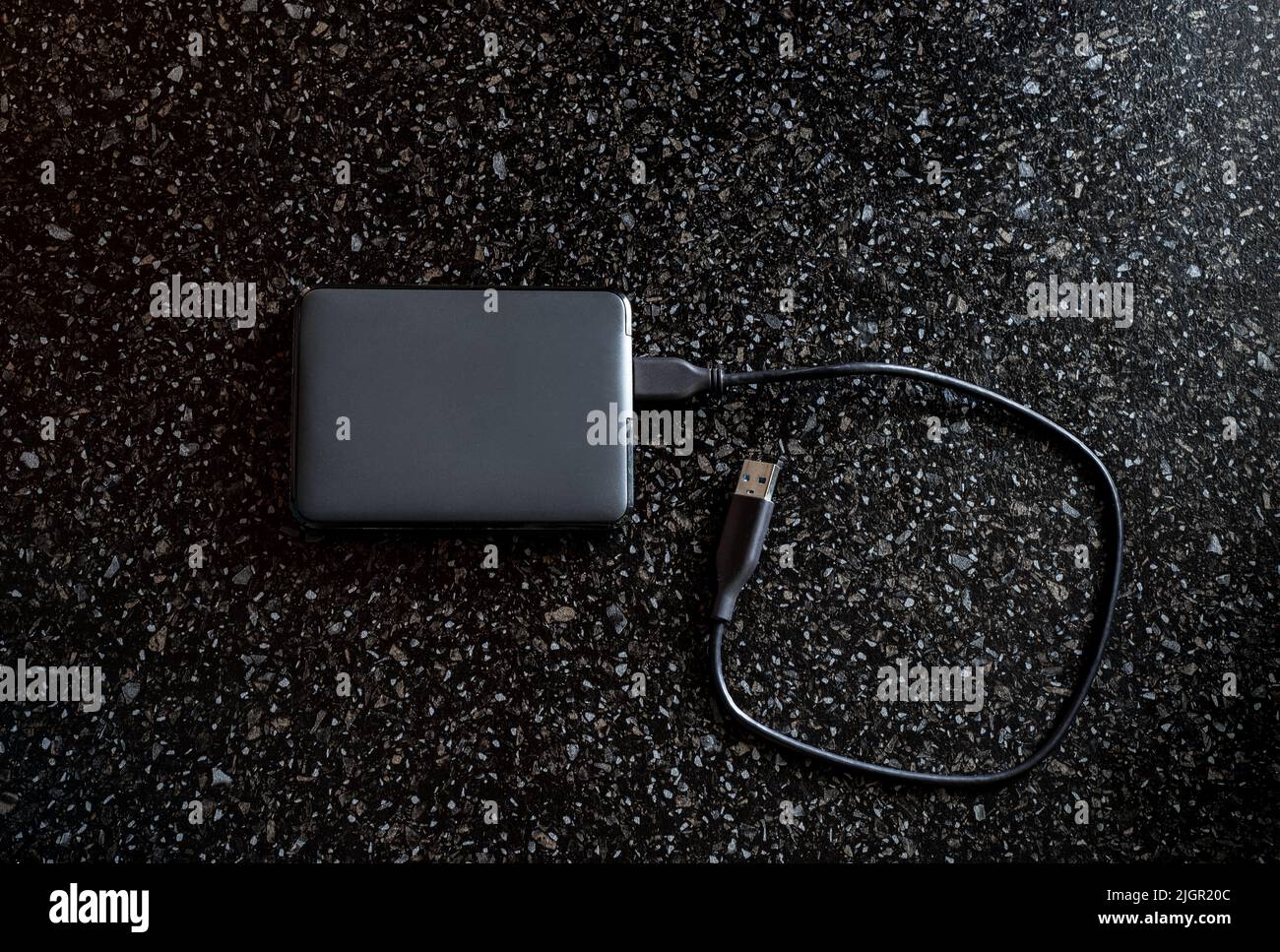 External hard drive in a black case with a wire on a black background. Useful portable storage device, high speed portable device. Stock Photo