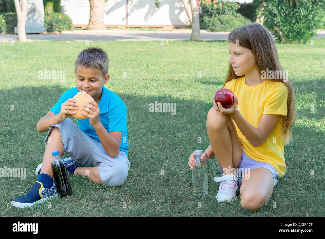 Children schoolchildren eat lunch in the park. Harmful and healthy food. Stock Photo