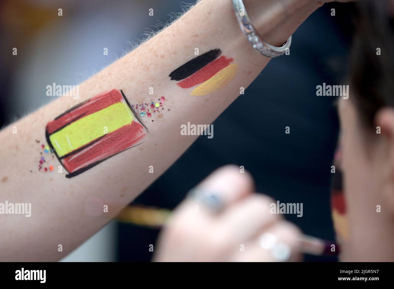 12 July 2022, Great Britain, Brentford/ London: Soccer, Women: European Championship, Germany - Spain, preliminary round, Group B, Matchday 2, Brentford Community Stadium. A fan gets the German national flag painted on his cheek before the match. Photo: Sebastian Christoph Gollnow/dpa Stock Photo