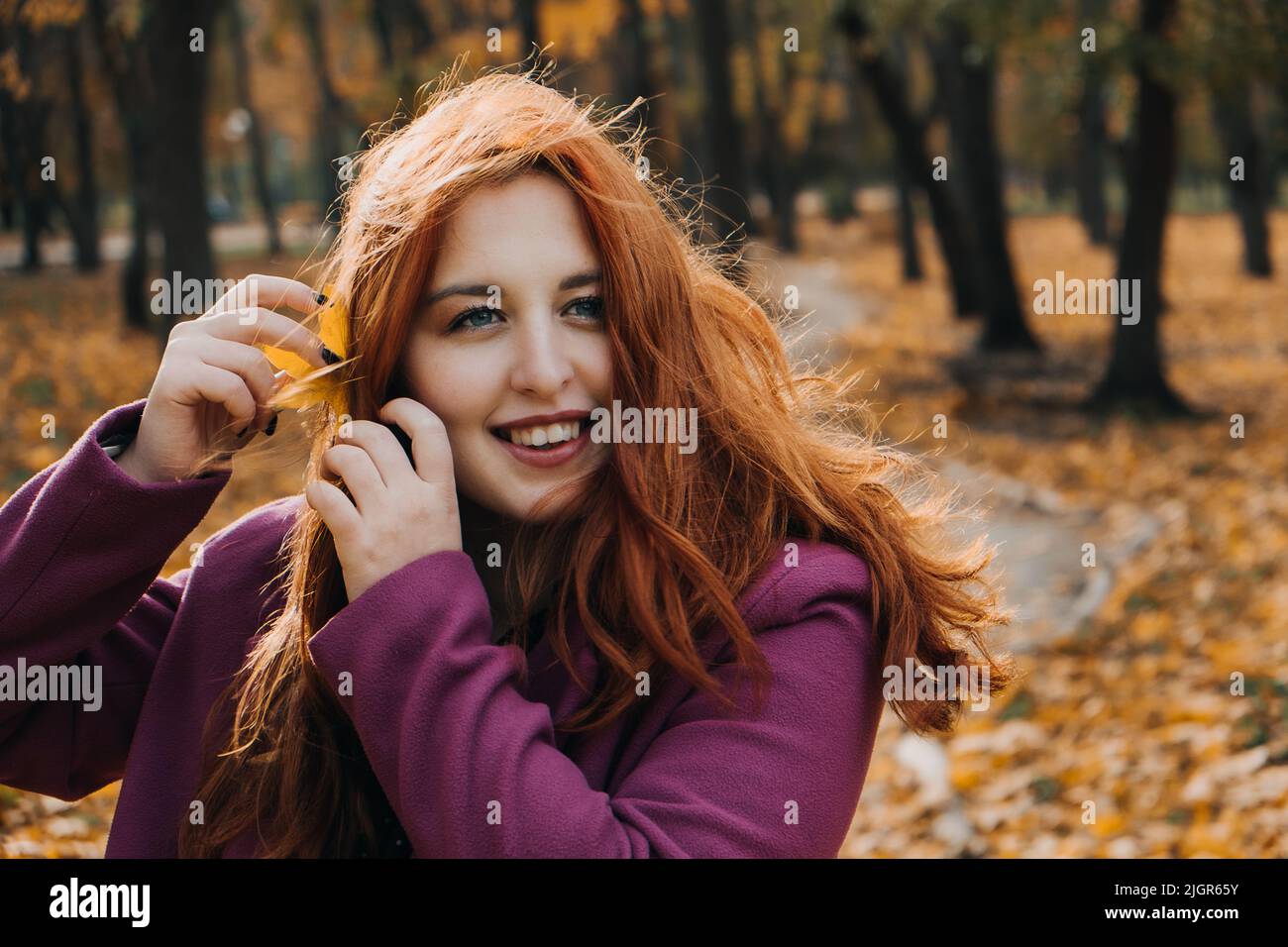 Autumn portrait of candid beautiful red-haired girl with fall leaves in hair. Stock Photo