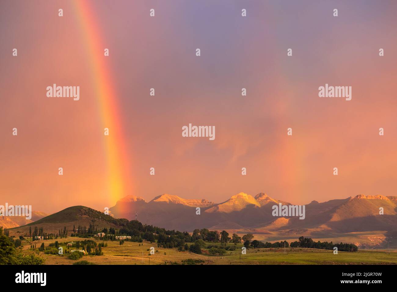 View of a double rainbow at sunset against a backdrop of mountains in the town of Clarens, South Africa, near the Golden Gate Highlands National Park Stock Photo