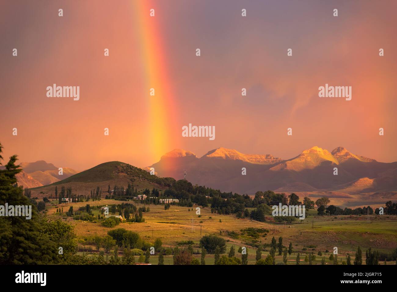 View of a rainbow at sunset against a backdrop of mountains in the town of Clarens, South Africa Stock Photo