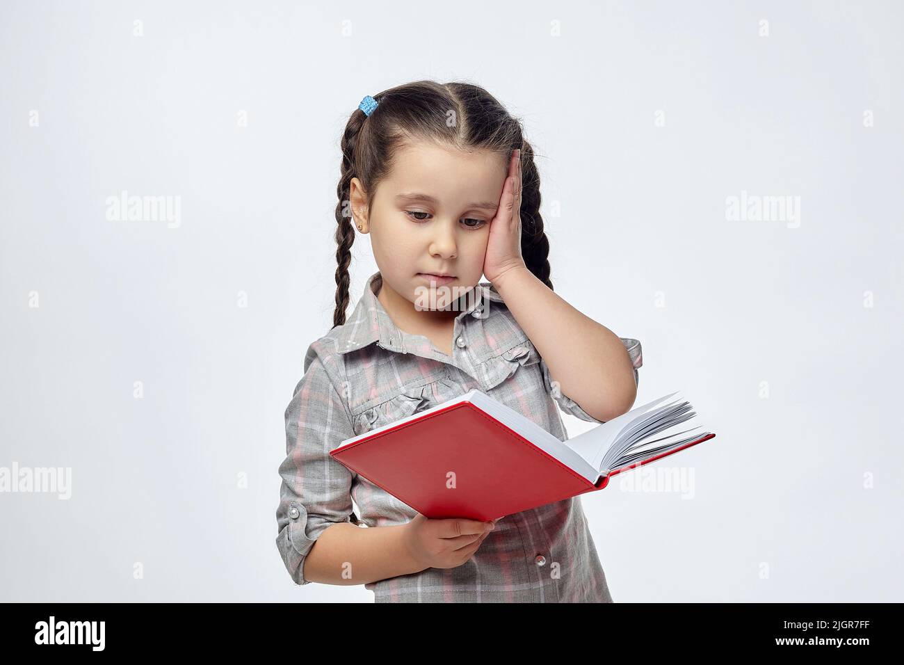 little blackhaired girl holds a red book and puts her hand to her head