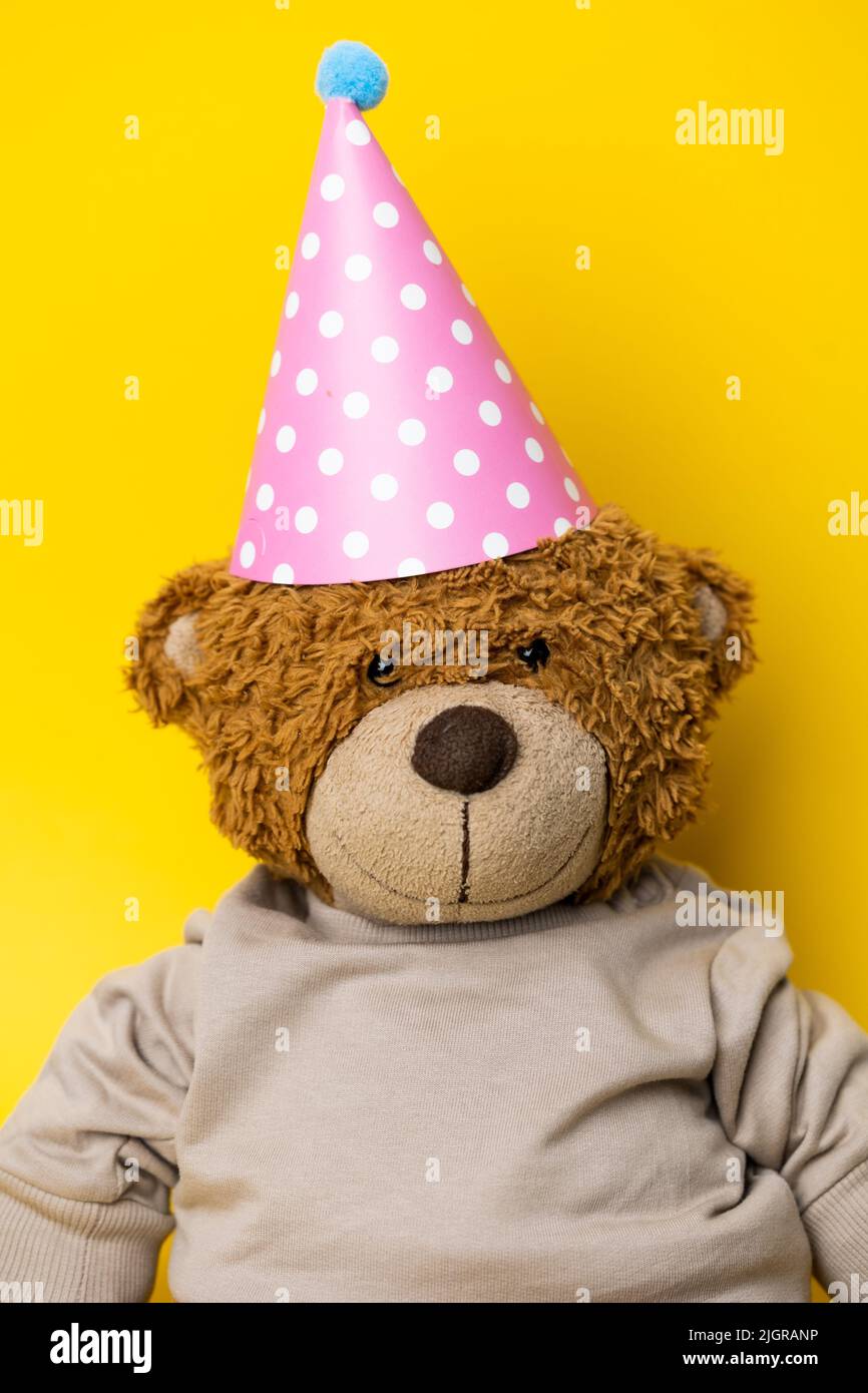 Cute Teddy Bear with a party hat. Adorable Teddy Bear celebrating. Smiling Teddy bear with a pullover. Party hat plush. Stock Photo