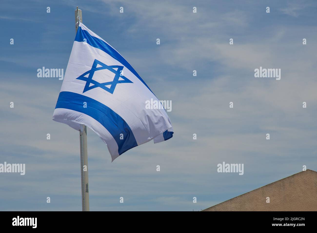 The flag of Israel on pole flutters in wind under blue sky. Israeli ...