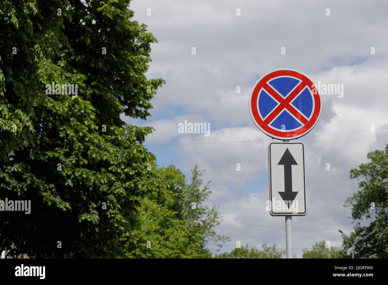 A European road sign indicating that stopping and parking is prohibited in front of and outside the sign. Blue sky and nature in the background. High Stock Photo