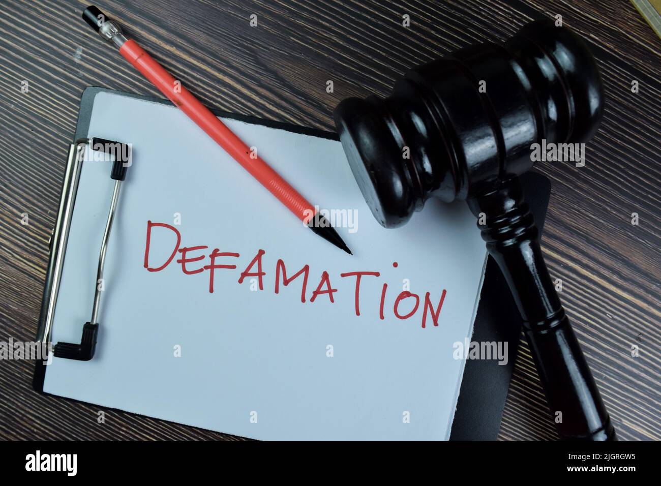 Concept of Defamation write on a paperwork isolated on Wooden Table. Stock Photo