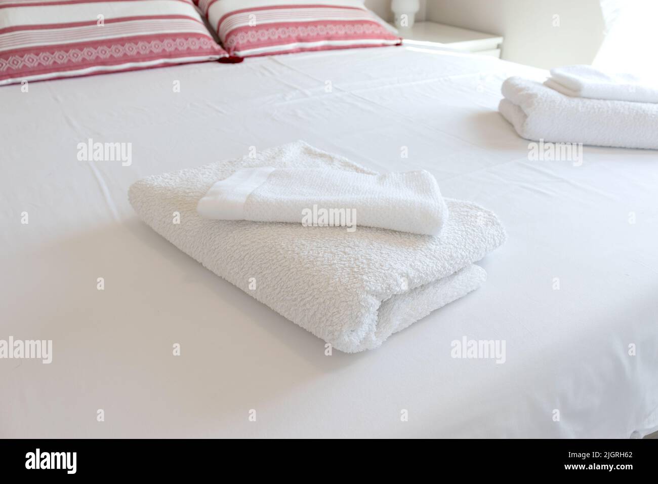 White folded towels on a hotel bed with white sheets. Stock Photo
