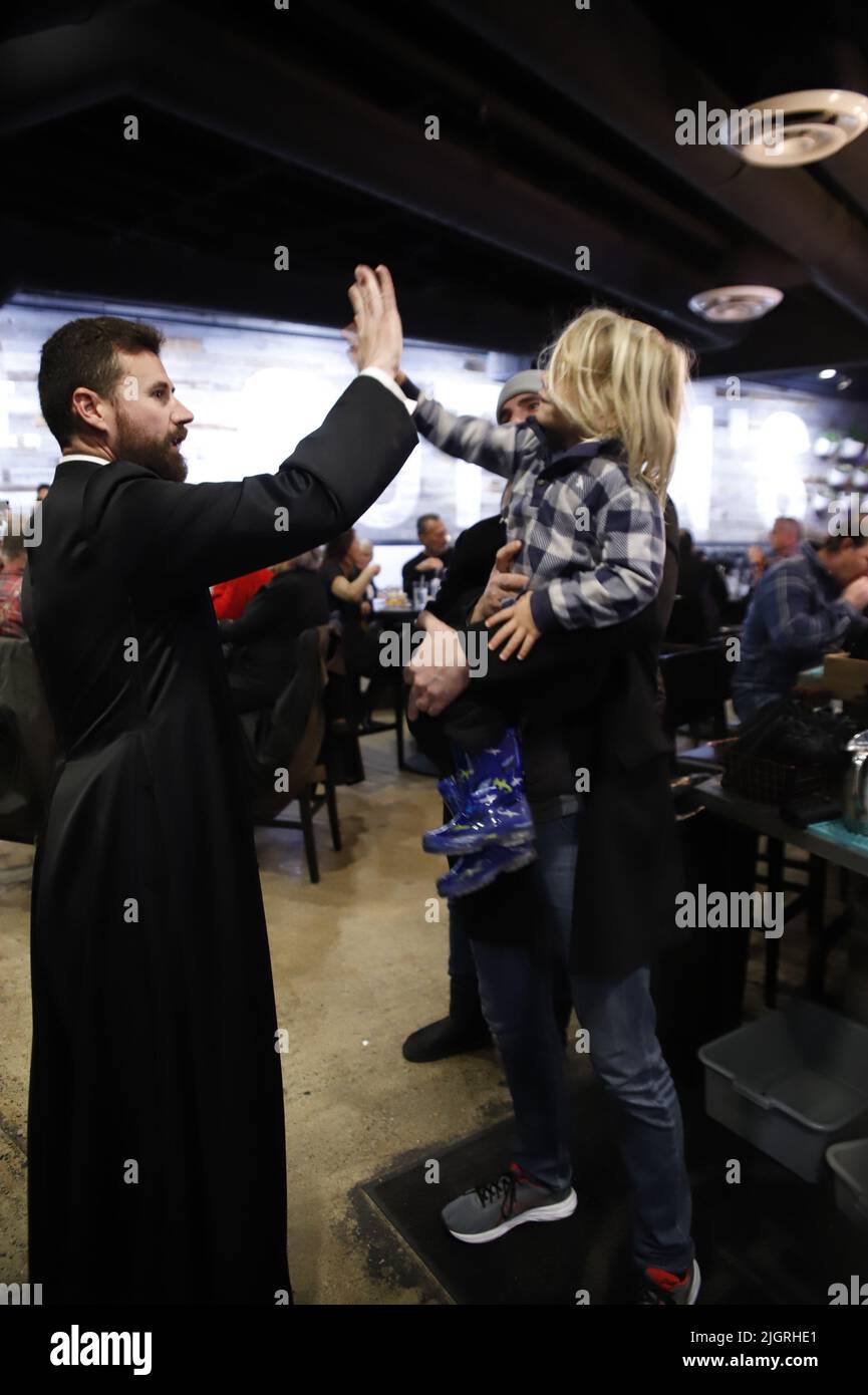 A bearded Catholic priest high-fives a little boy at an informal church entertainment in San Clemente, CA Stock Photo