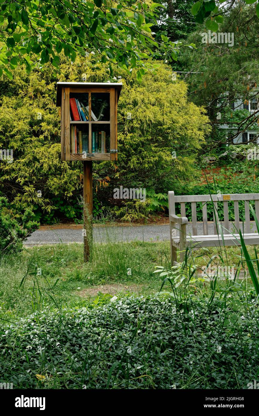 A free library box stands next to a wooden bench in a park at the Acton