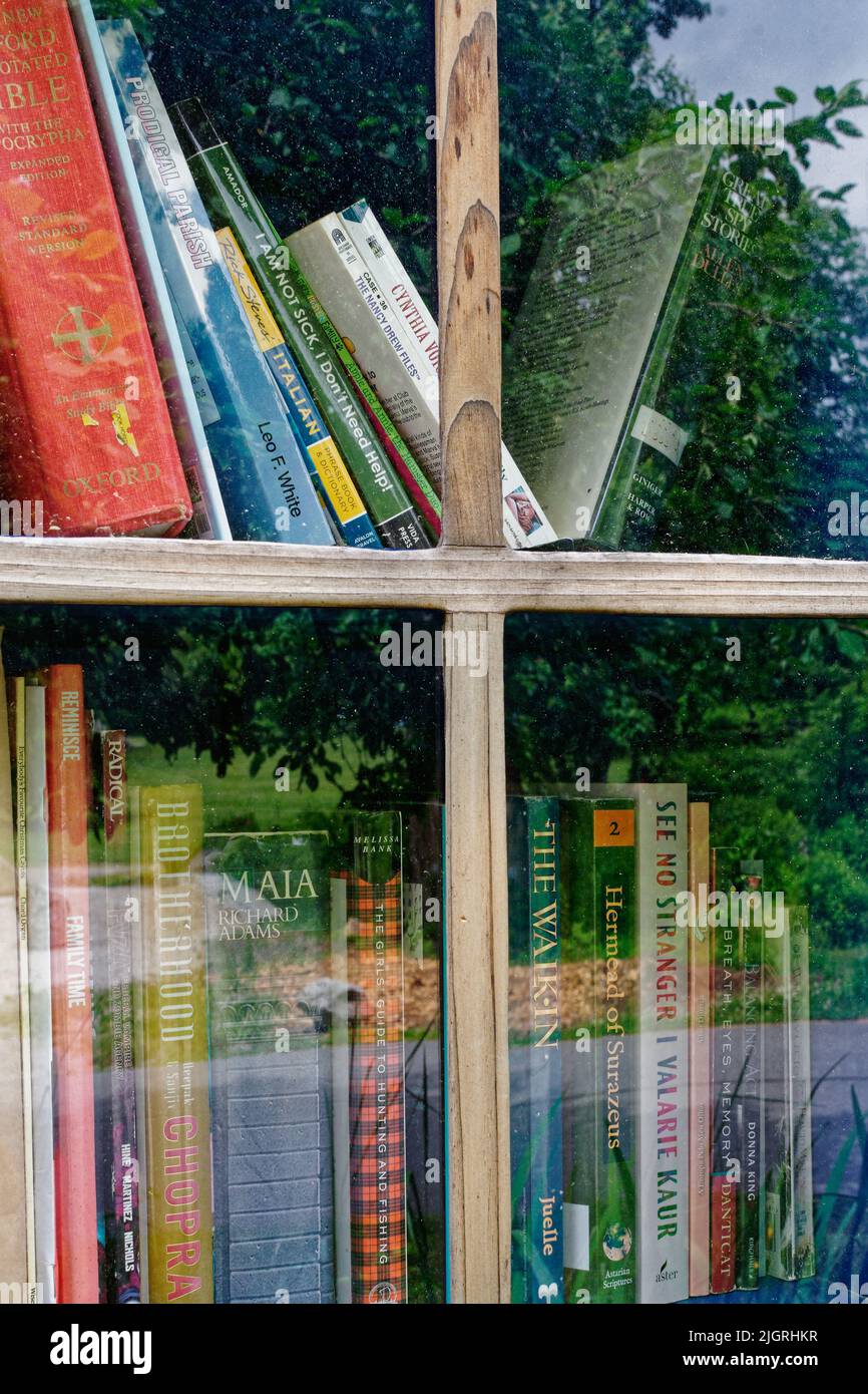 A free library box stands next to a wooden bench in a park at the Acton