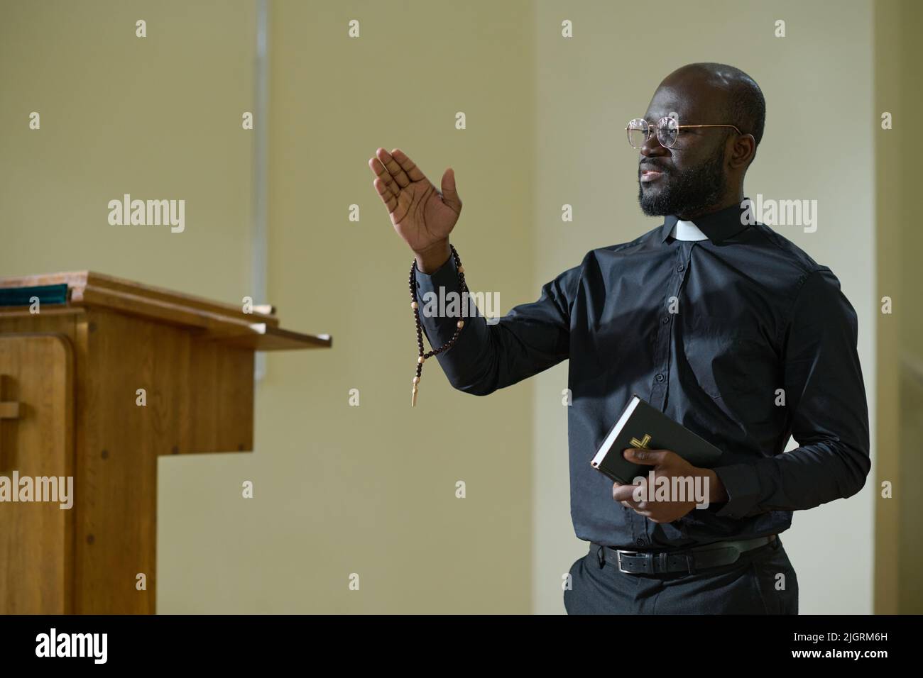 Confident African American man in pastor apparel with clerical collar preaching during church service in front of parishioners Stock Photo