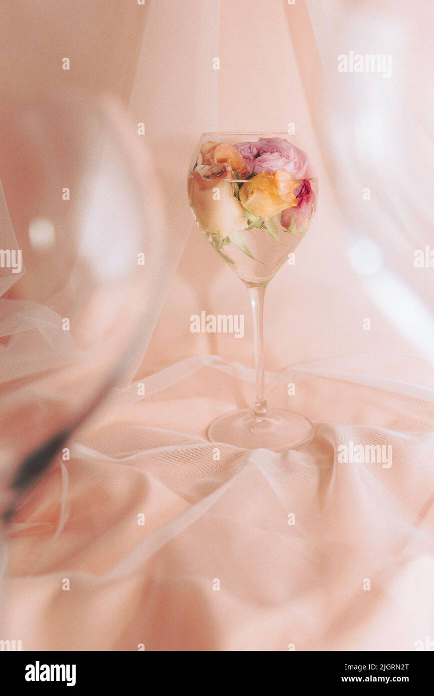 A vertical shot of a glass of water with colorful rose buds on a silky cloth Stock Photo