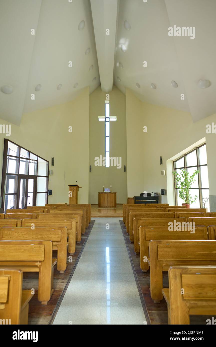 Interior of modern Catholic church with two rows of wooden benches for parishioners and long aisle leading to pulpit with cross above Stock Photo