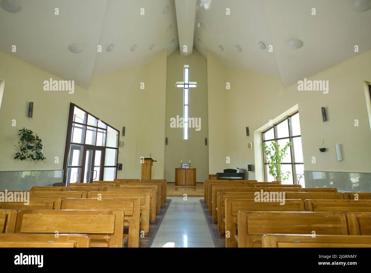 Empty hall for church services with aisle between two rows of wooden benches for parishioners and cross above pulpit of pastor Stock Photo