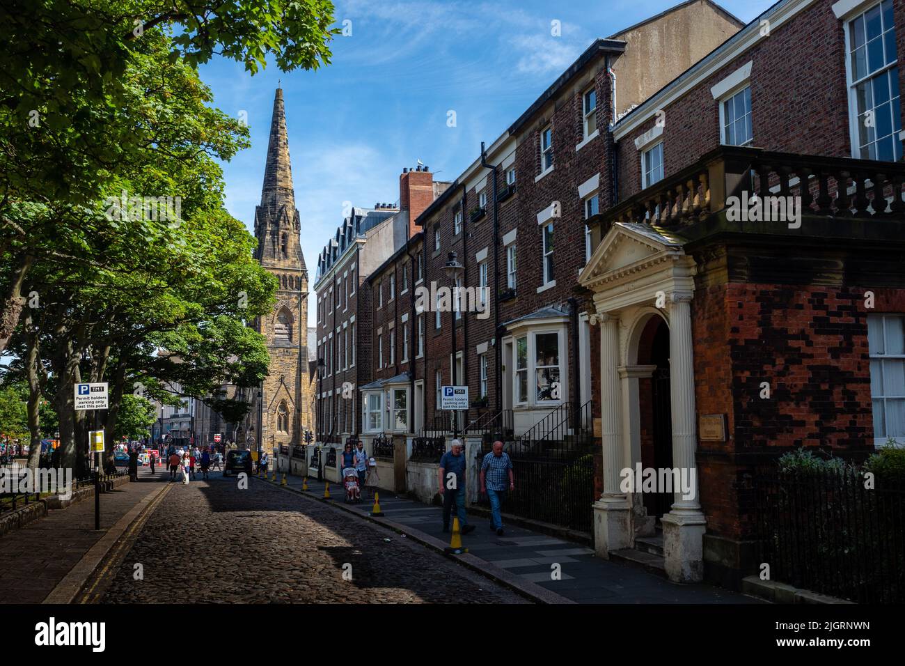 Cobbled residential street in Tynemouth, North Tyneside, UK - townhouses, with church and park with leafy trees Stock Photo
